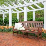 Poly bench on brick pathway thru flower garden under white pergola