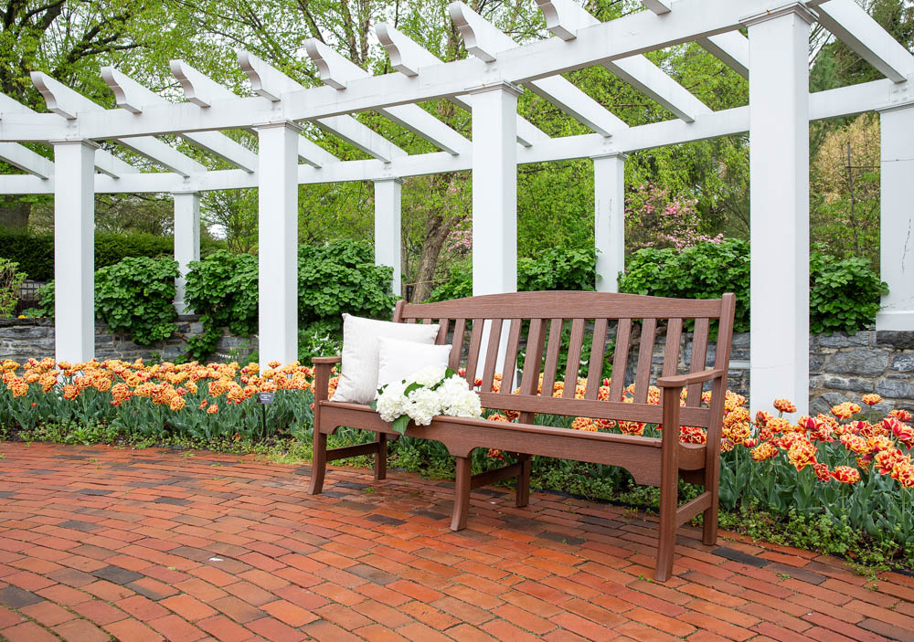 Poly bench on brick pathway thru flower garden under white pergola