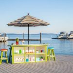 Amish crafted poly bar and bar stools on waterfront boardwalk with boats docked in background.
