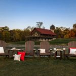 Poly adirondack chairs and accent tables sit on pond bank with lodge in background