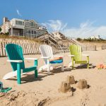 3 poly Adirondack chairs sit in sand on beach