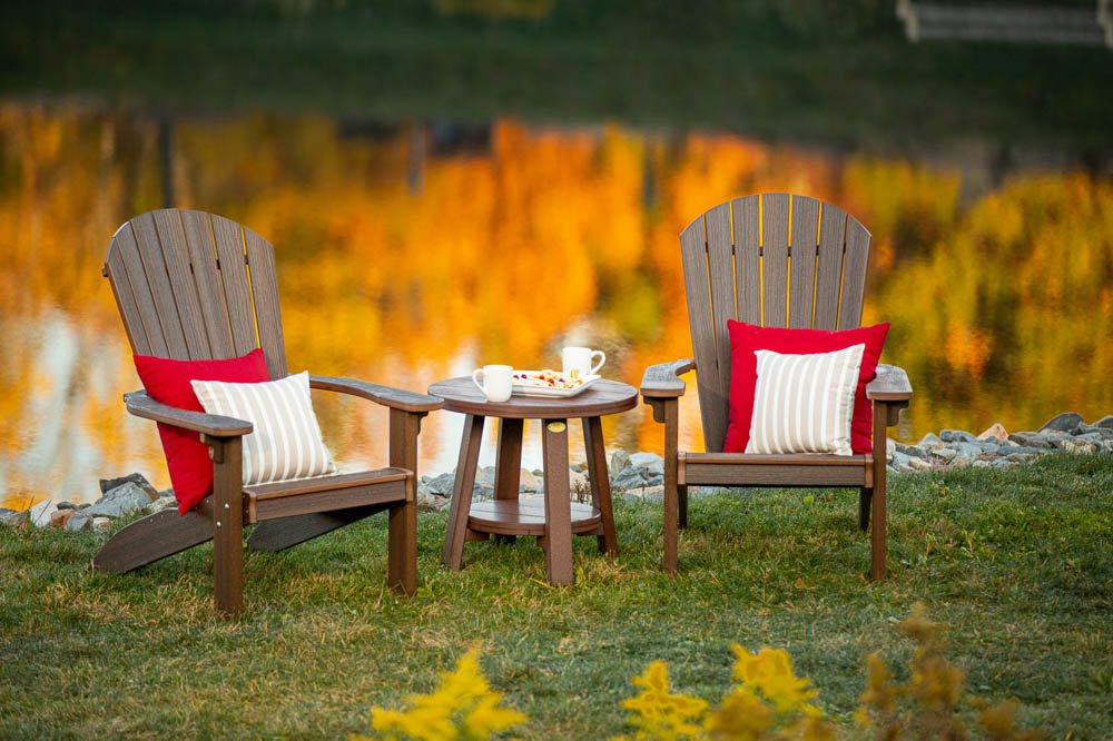 Two outdoor poly adirondack chairs by a lake