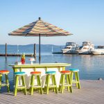 Poly bar and bar stools on waterfront boardwalk with boats at anchor in background
