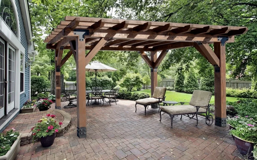 Timberview Pergola crafted from Douglas fir, featuring heavy timber beams and black steel bracket hardware over a brick paver patio with lounge seating and a lush garden backdrop.